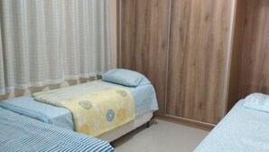 Un dormitorio con dos camas, un armario de madera y un ventilador blanco.
