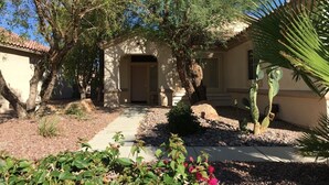 Une maison avec un chemin de pierres menant à une porte en bois, entourée de cactus et de plantes du désert.