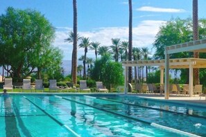 Una piscina con agua azul cristalina, rodeada de sillas de descanso y palmeras.