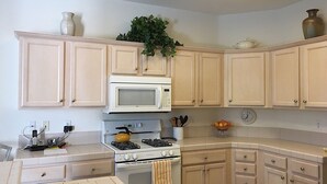 Une cuisine avec des meubles de couleur beige, un four à micro-ondes blanc, une cuisinière à gaz et un évier.