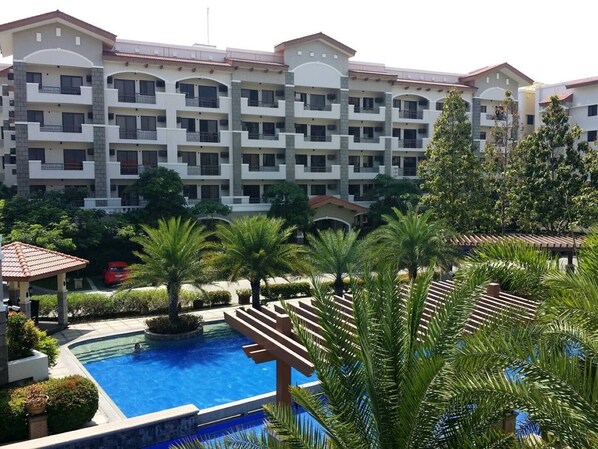 Experience the hotel's sleek, multi-story design with balconies on every floor, overlooking a serene pool surrounded by lush greenery.