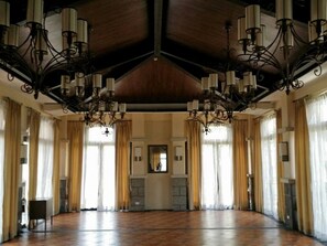 Spacious room with a high ceiling and open floor plan, featuring a polished floor and large windows with sheer curtains.