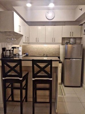 Compact kitchen with a central island, featuring a stainless steel refrigerator, cabinets, and a clock.