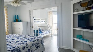 A bedroom with a bunk bed, a white dresser, a TV on a shelf, and a ceiling fan. - Location, Location, Location! (Surfside Beach)