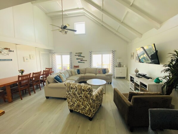 A spacious living room with a high ceiling, a ceiling fan, a large window, a sofa, a coffee table, and a TV mounted on the wall. - Moondancer - Beach views, spacious , pet friendly! (Surfside Beach)
