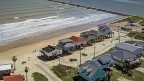 A coastal town with beachfront properties, a pier extending into the water, and a clear sky. - Location, Location, Location! (Surfside Beach)