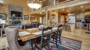 A spacious dining area with a wooden table and chairs, a fireplace, and a television mounted on the wall.
