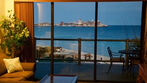 Ein Zimmer mit großem Fenster mit Blick auf einen Strand und eine entfernte Insel.