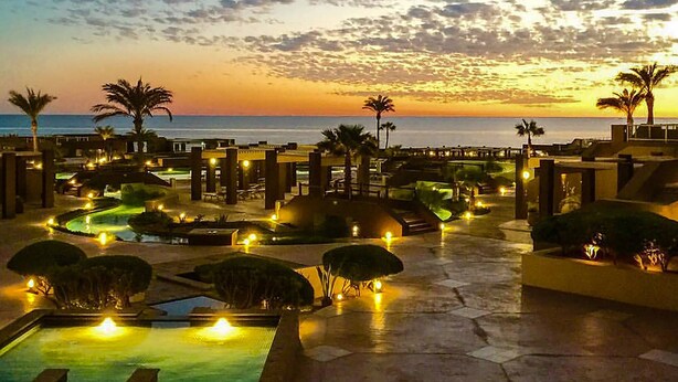 Ein Poolbereich eines Resorts mit mehreren Pools und Palmen, umgeben von Gebäuden mit warmer Beleuchtung.