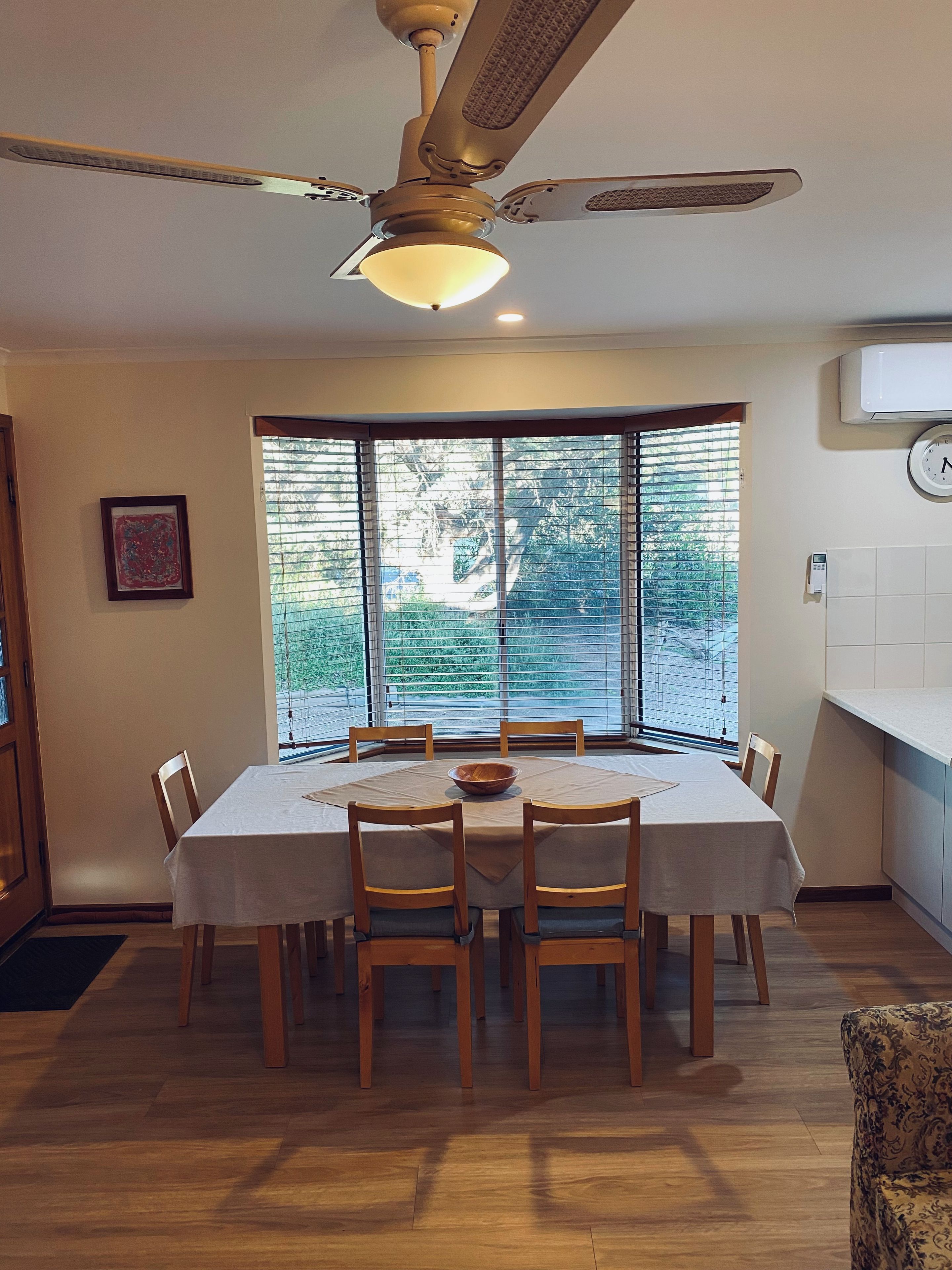Un coin repas avec une table dressée pour six personnes, un ventilateur de plafond et une vue dégagée grâce à de grandes fenêtres.