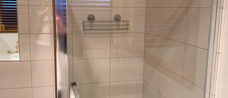 Une douche fermée par des parois en verre, dotée d’un pommeau de douche à main et d’un robinet mural.