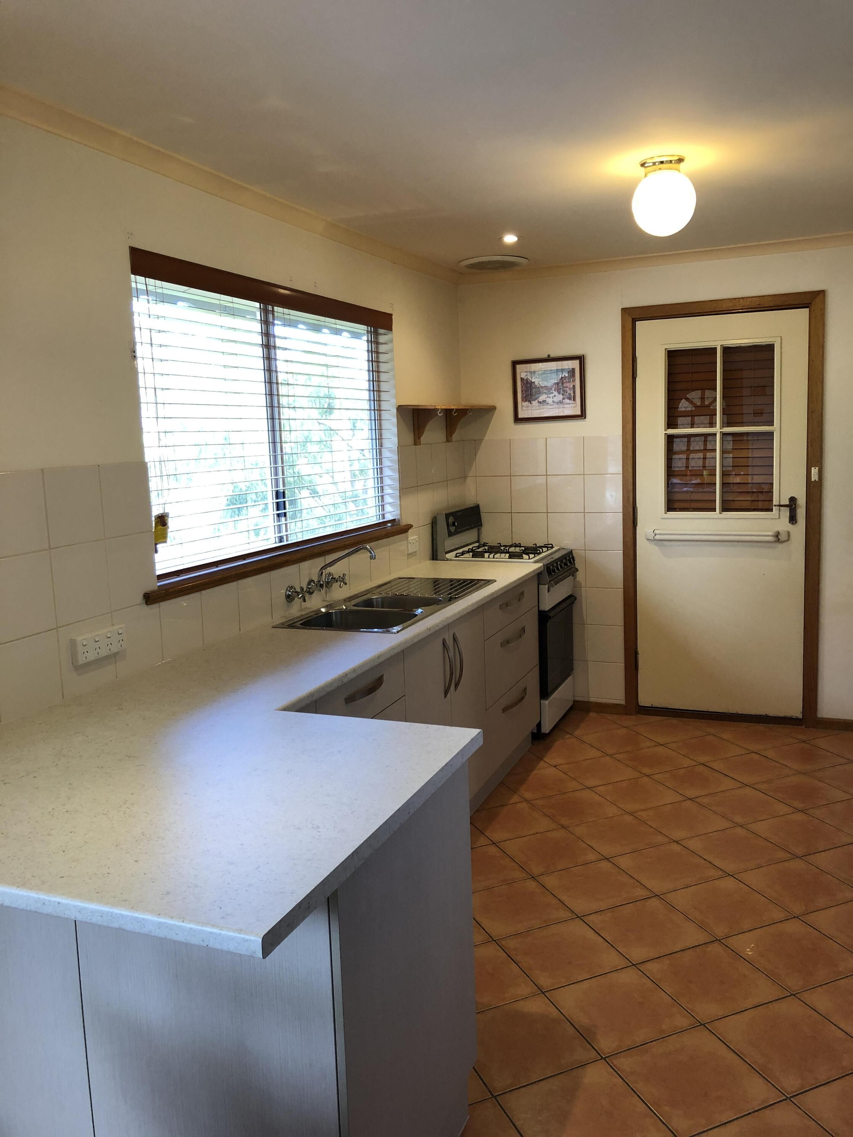 A kitchen with a central island, a window with blinds, a stove, and a door with a window.