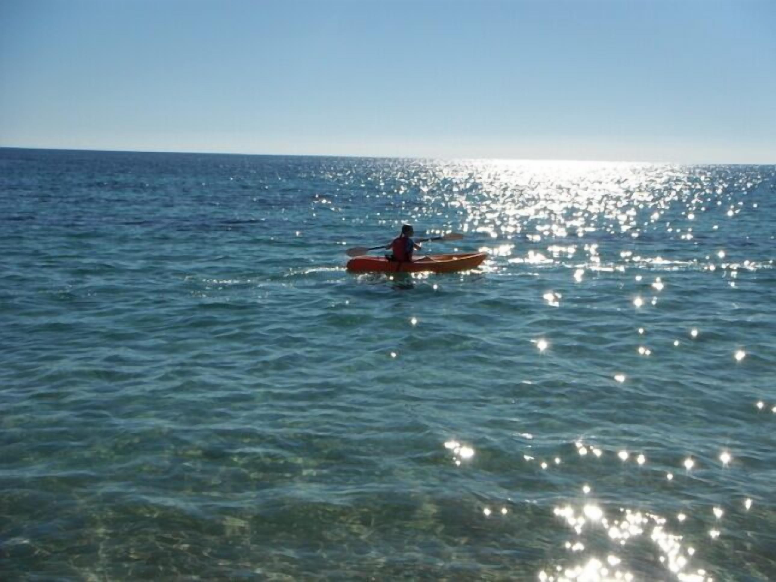 Una persona practica kayak en un mar tranquilo, con el sol reflejándose en el agua.