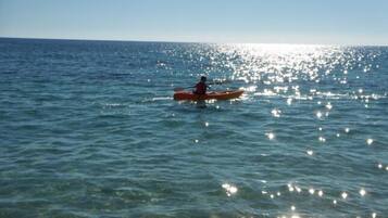 Una persona practica kayak en un mar tranquilo, con el sol reflejándose en el agua.