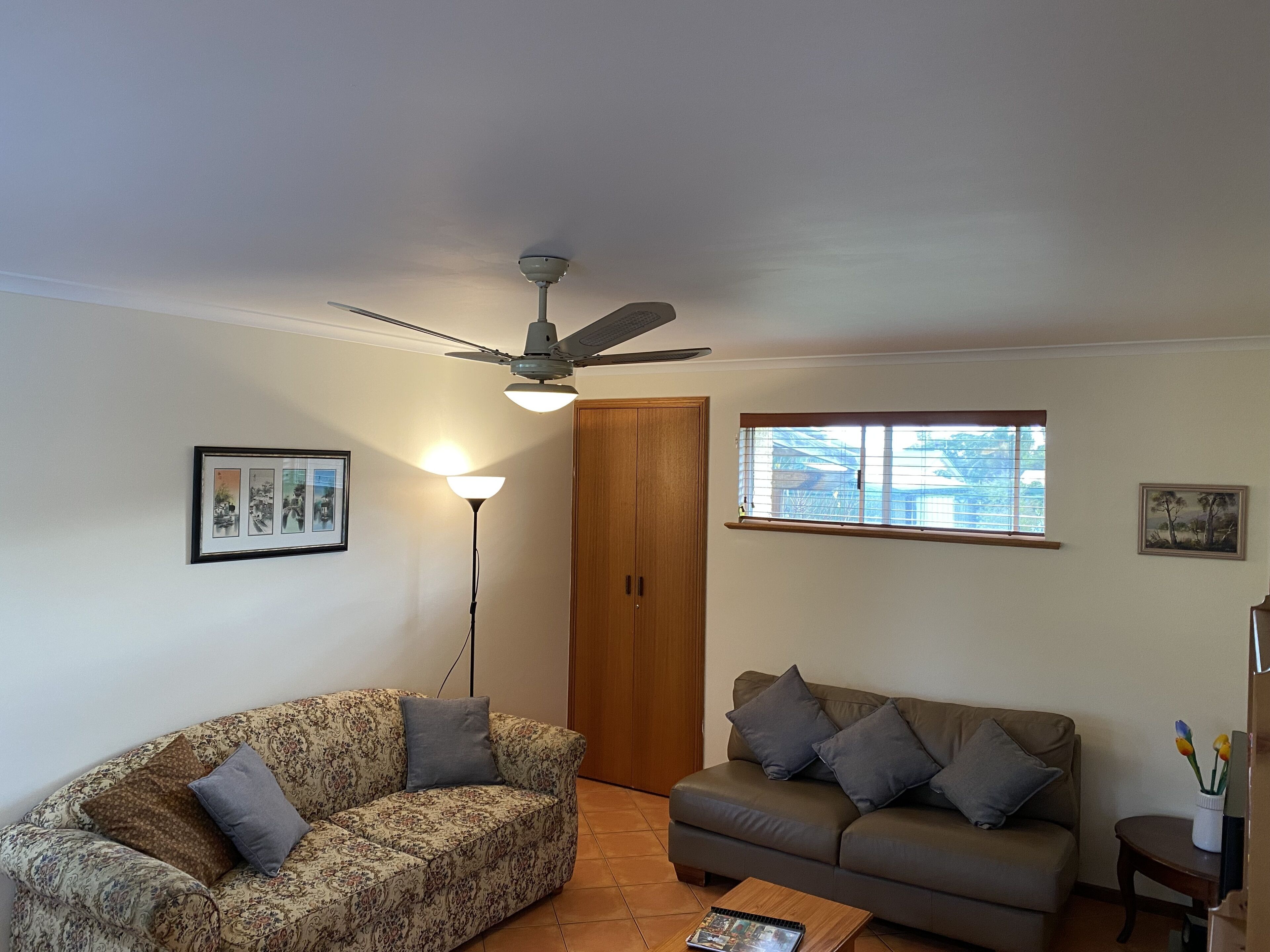 Ein Wohnzimmer mit zwei Sofas, einem Deckenventilator, einer Stehlampe und einem Fenster mit Jalousien.
