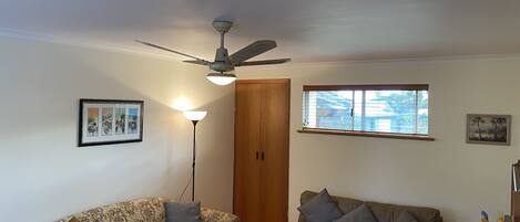 Ein Wohnzimmer mit zwei Sofas, einem Deckenventilator, einer Stehlampe und einem Fenster mit Jalousien.