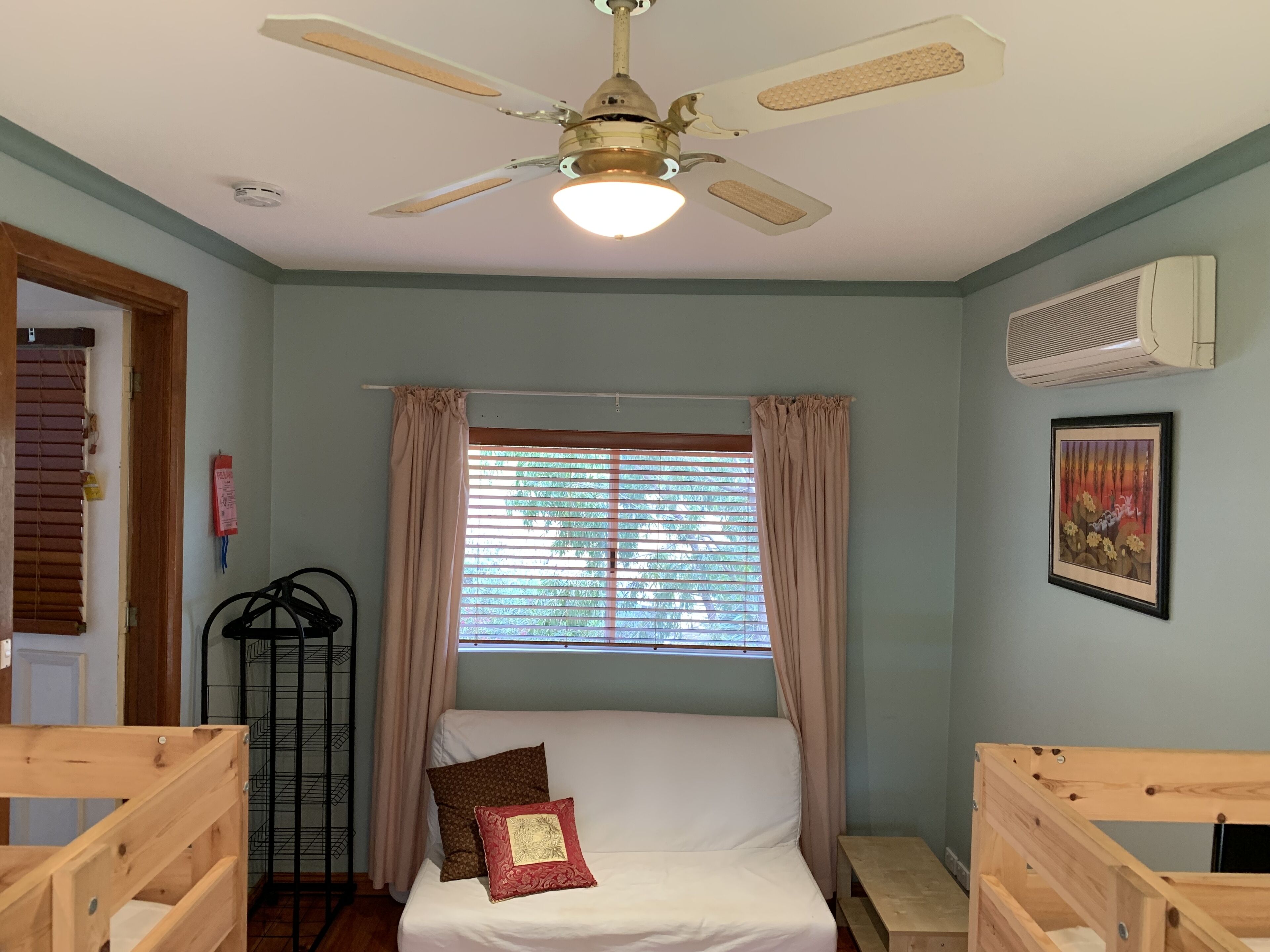 A bedroom with a bed, a ceiling fan, a window with curtains, a wall-mounted air conditioner, and a framed picture.