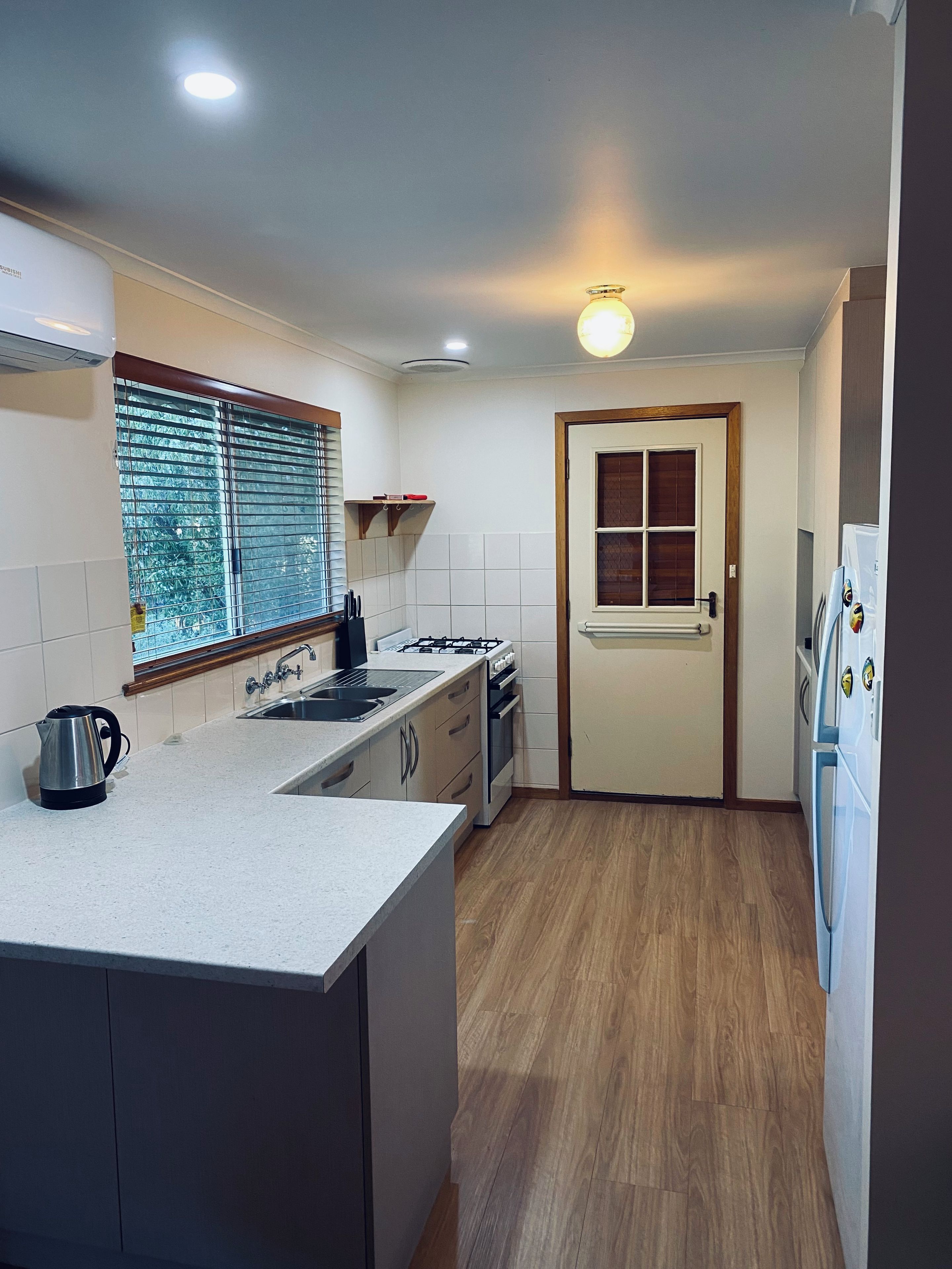 A compact kitchen with a central island, a window with blinds, a built-in oven, and a refrigerator.