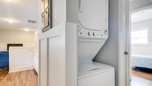 Un cuarto de lavado con lavadora y secadora, un sofá azul y una cama en la habitación contigua.