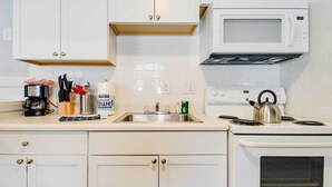 Una cocina con armarios blancos, microondas, hervidor de agua y cafetera.