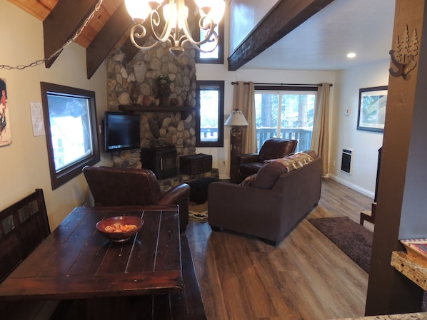 A cozy living room with a stone fireplace, a television, a dining table with a bowl of food, and a comfortable sofa.