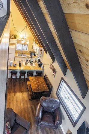 A cozy loft-style room with a dining area, a kitchen, and a seating area with a view of the outdoors.