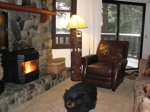 A cozy living room with a stone fireplace, a leather armchair, and a bear plush toy on the floor.