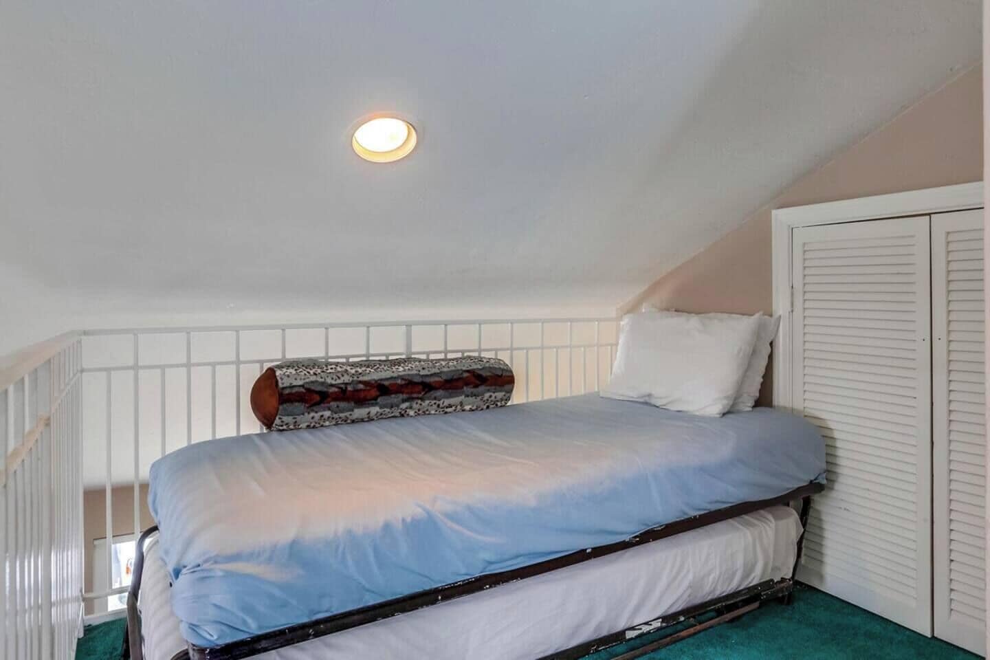 A single bed with a headboard, white walls, a ceiling light, and a window with blinds.