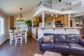 A spacious living room with a dark leather sofa and a dining area with white chairs. - Balcony Ocean view, heart of MB, garage and bikes (San Diego)