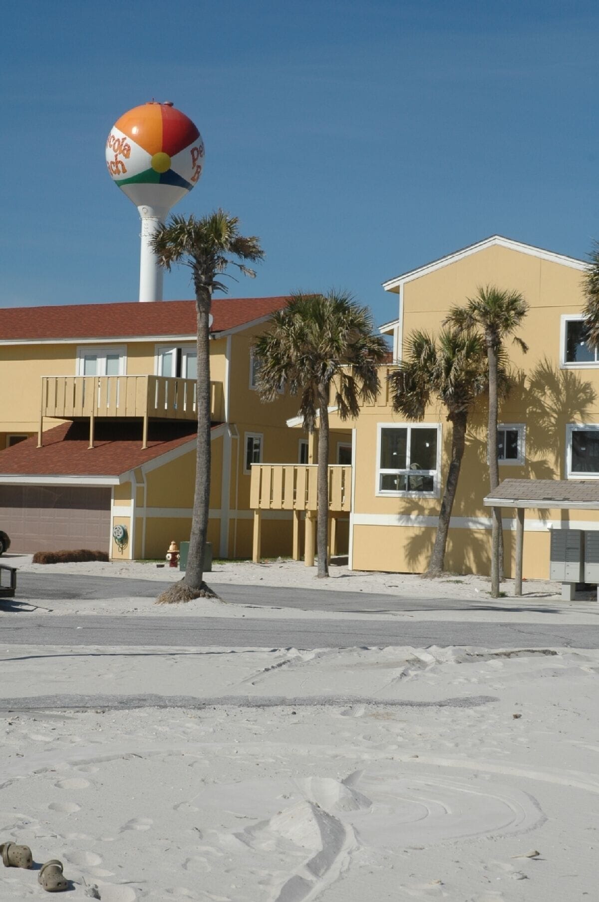 Un edificio frente a la playa con un colorido adorno de pelota de playa, palmeras y cielo despejado.