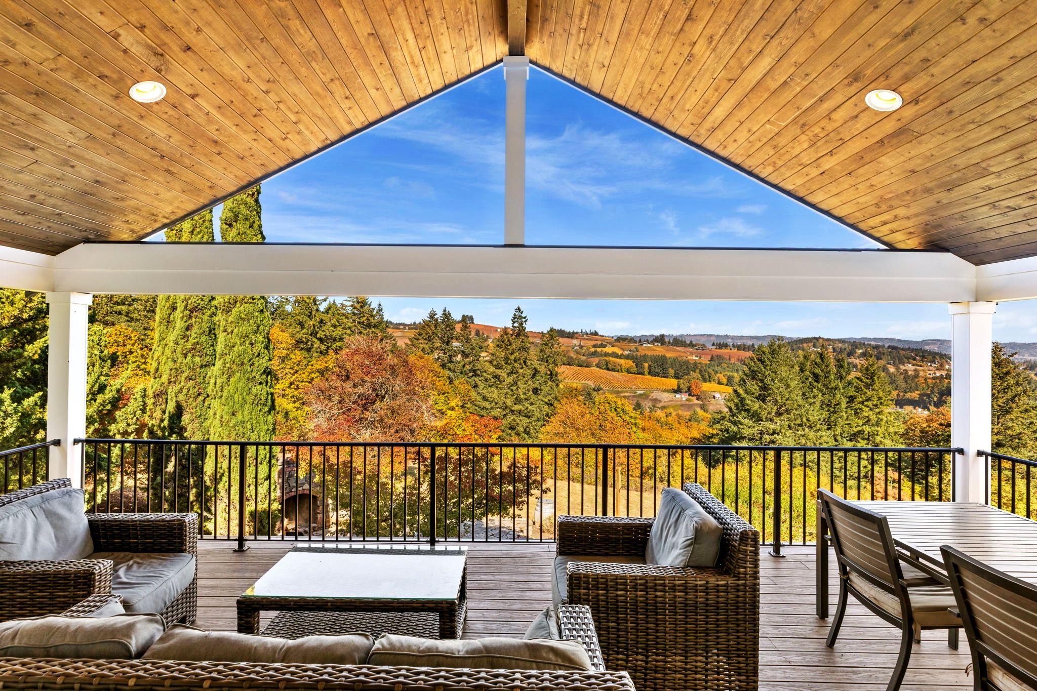 A covered outdoor seating area with wicker furniture and a view of a landscape with trees and hills.