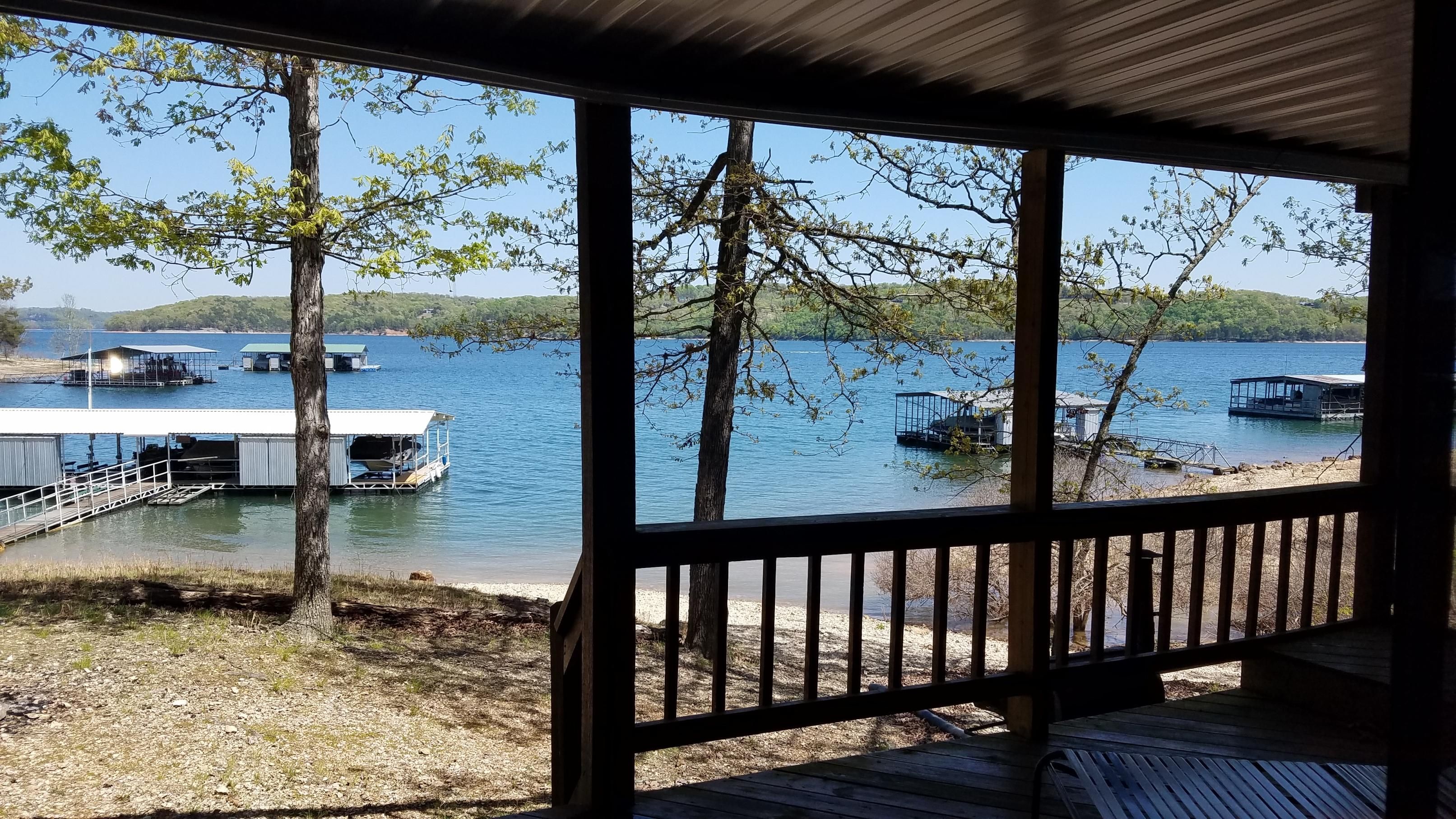 Une terrasse couverte offrant une vue sur un lac, des bateaux amarrés et un petit bâtiment.