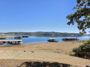 Une zone au bord du lac où sont amarrés des bateaux, une jetée surmontée d’une structure couverte, et une vue dégagée sur le lac et les collines lointaines.