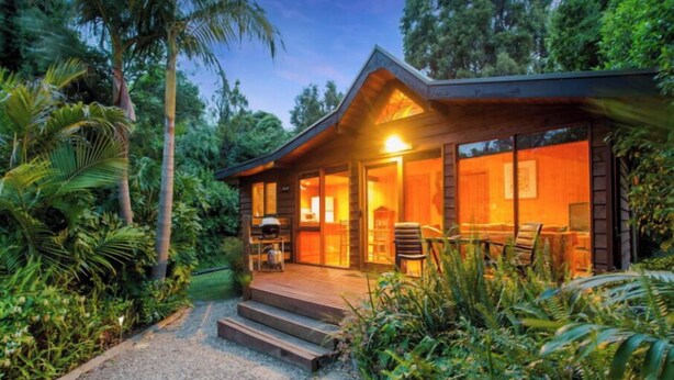 Een gezellig houten vakantiehuisje, met een veranda en buitenzitplaatsen, en een grindpad naar de ingang.