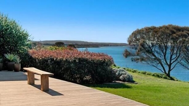 Een houten terras met een bankje met uitzicht op een meer, omringd door groen en een heldere lucht.
