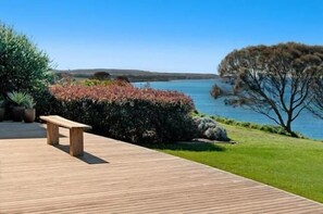 Une terrasse en bois avec un banc donnant sur un lac, entourée de verdure et sous un ciel dégagé.
