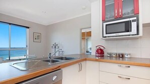 Een moderne keuken met een spoelbak van roestvrij staal, een magnetron en houten keukenkastjes.