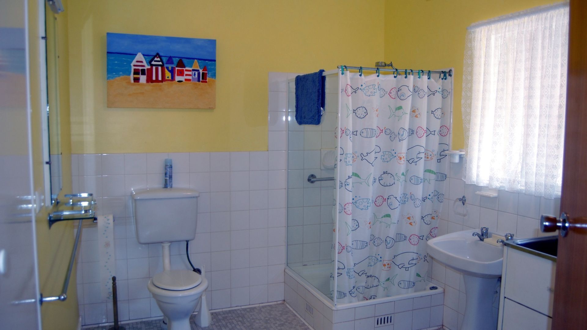A bathroom with a toilet, sink, shower, and a painting on the wall.