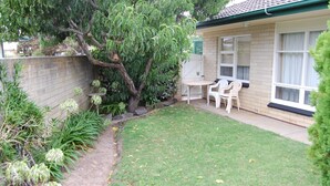 Een kleine achtertuin met gazon, boom en terras met twee stoelen.