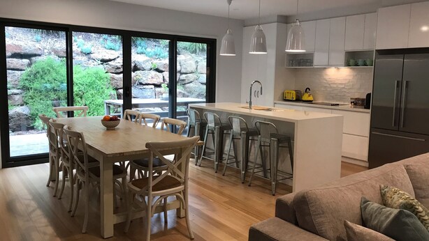 A modern kitchen with a central island, bar stools, and a dining table with chairs. - The Boulevard House Lorne (Lorne)