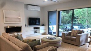 A modern living room with a sofa, armchairs, a flat-screen TV, and a sliding glass door to a balcony. - The Boulevard House Lorne (Lorne)