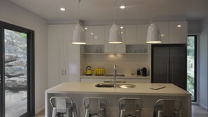 A modern kitchen with a central island, pendant lights, and a large window. - The Boulevard House Lorne (Lorne)