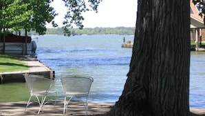 Un banc au bord du lac, sous un arbre, une jetée avec un bateau, et une rive lointaine.