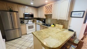 Cocina con refrigerador de acero inoxidable, microondas, horno y lavavajillas. Hay una isla grande con cubierta decorada.