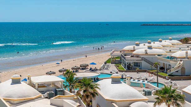 Un complejo turístico con varias construcciones de cúpulas blancas, una playa y una zona de piscina.