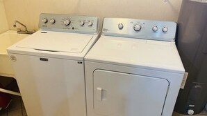 Dos lavadoras Maytag de carga frontal blancas en un cuarto de lavado con un lavamanos blanco y un refrigerador de acero inoxidable.