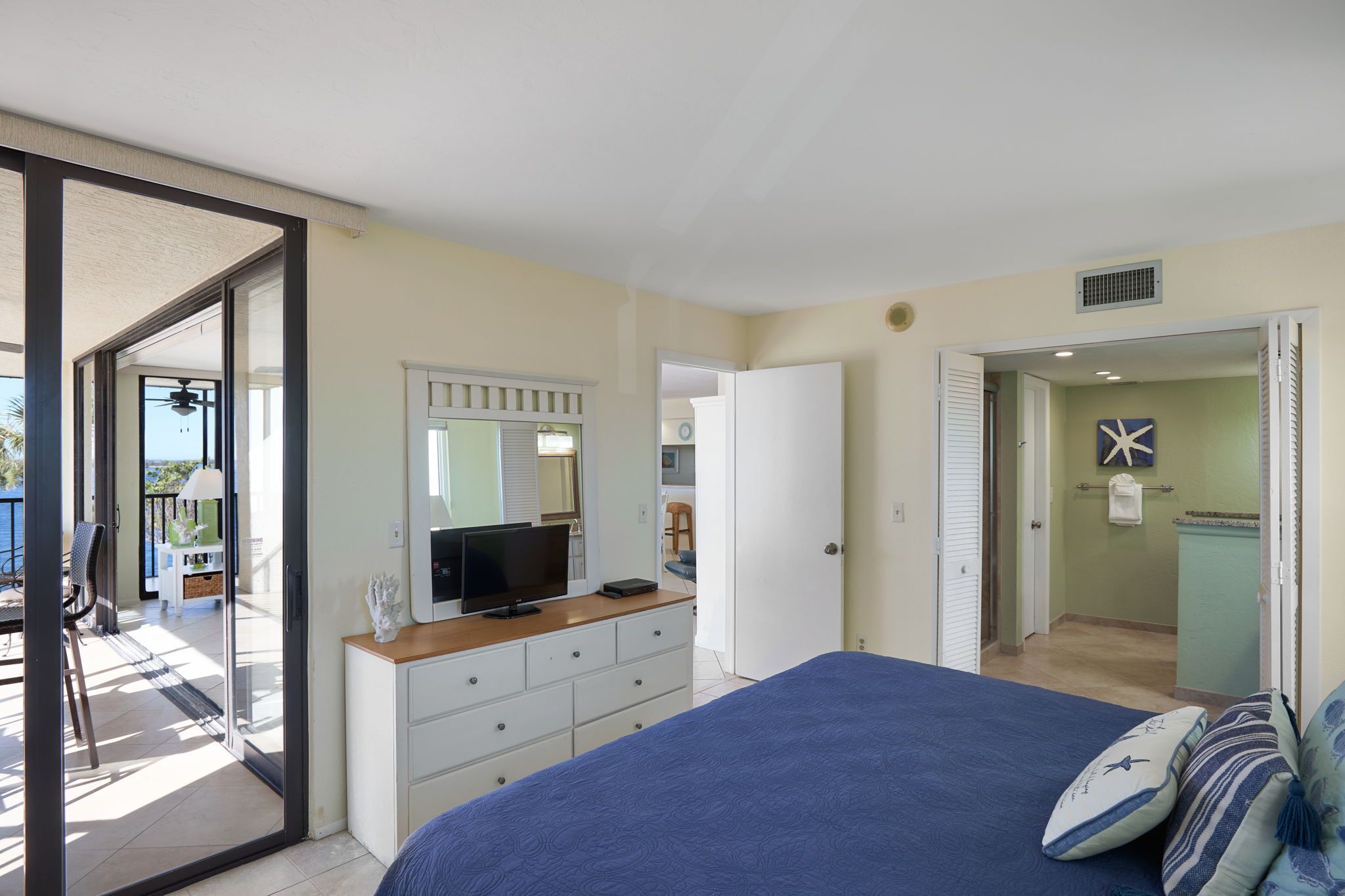 A bedroom with a large bed, a television, a dresser, and a sliding glass door leading to a balcony.