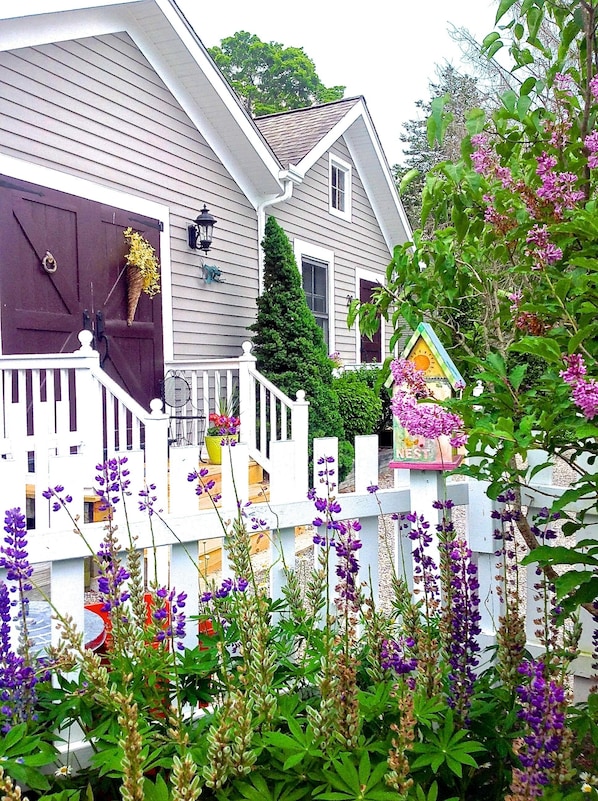 A house with a white picket fence, a front porch, and purple flowers in the foreground.