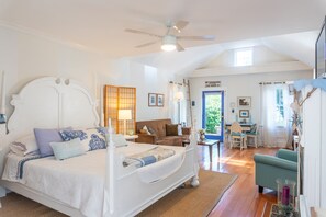 A spacious bedroom with a large bed, a ceiling fan, and a view of the dining area.