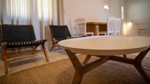 A round table with a wooden base, two wicker chairs, a white dining table, and a white chair in a room with a beige carpet.